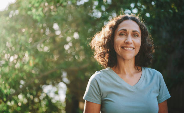 Smiling mature woman standing in a park outdoors in the summertime Portrait of a mature woman in sportswear smiling outside in a park on sunny day in summer Happy people stock pictures, royalty-free photos & images